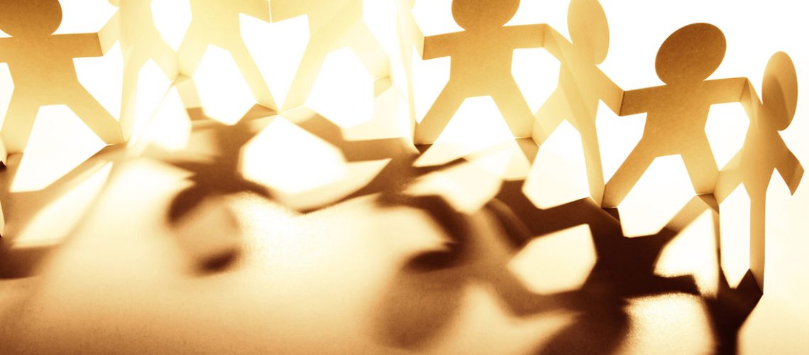 Paper dolls connected by the hands to demonstrate community